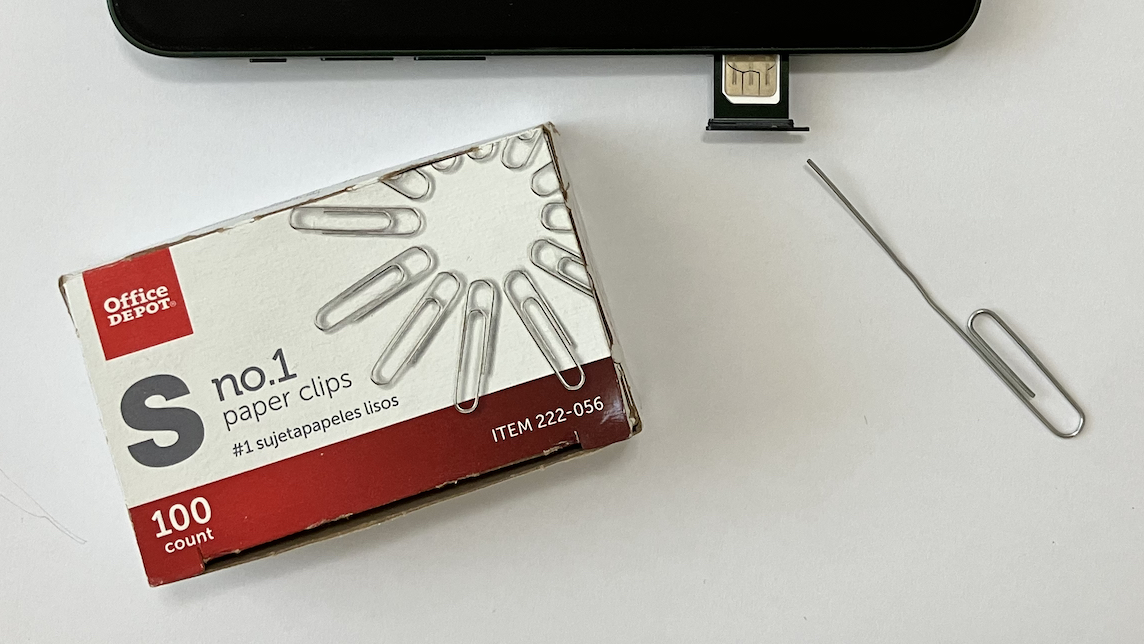 A box of paperclips, one paperclip with an end unfolded so that it sticks out straight, the half-opened subscriber information module tray of a cell phone, and the metal contacts of the SIM card